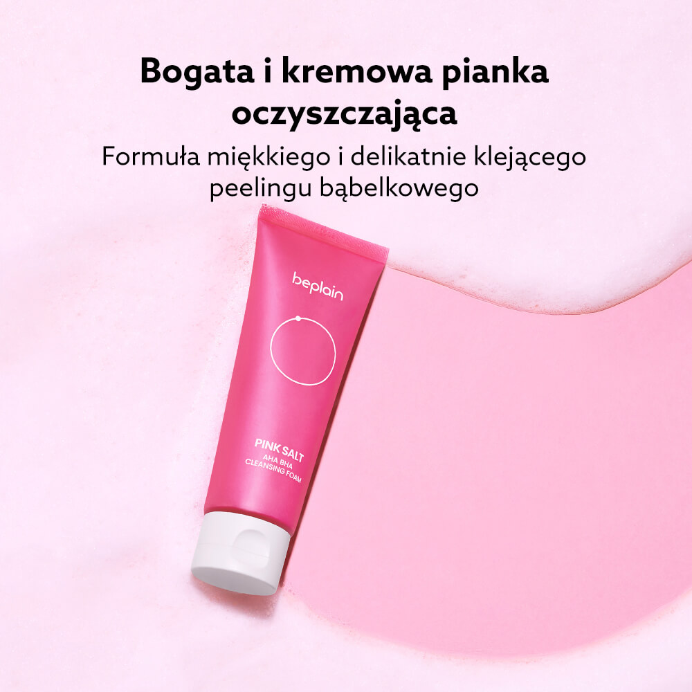 Beplain Pink Salt AHA BHA Cleansing Foam - tuba różowej pianki oczyszczającej leżąca na jasnoróżowej powierzchni pokrytej bąbelkową pianą, z hasłem o kremowej formule i peelingu bąbelkowym